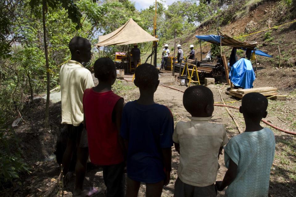 In this April 10, 2012 photo, children watch workers drill for gold, copper and silver at a temporary mountainside platform in the department of Trou Du Nord, Haiti. Haiti's land may yet hold the solution to centuries of poverty: there is gold hidden in its hills, and silver and copper too. Now, two mining companies are drilling around the clock to determine how to get those metals out, and how much it might cost.  (AP Photo/Dieu Nalio Chery)