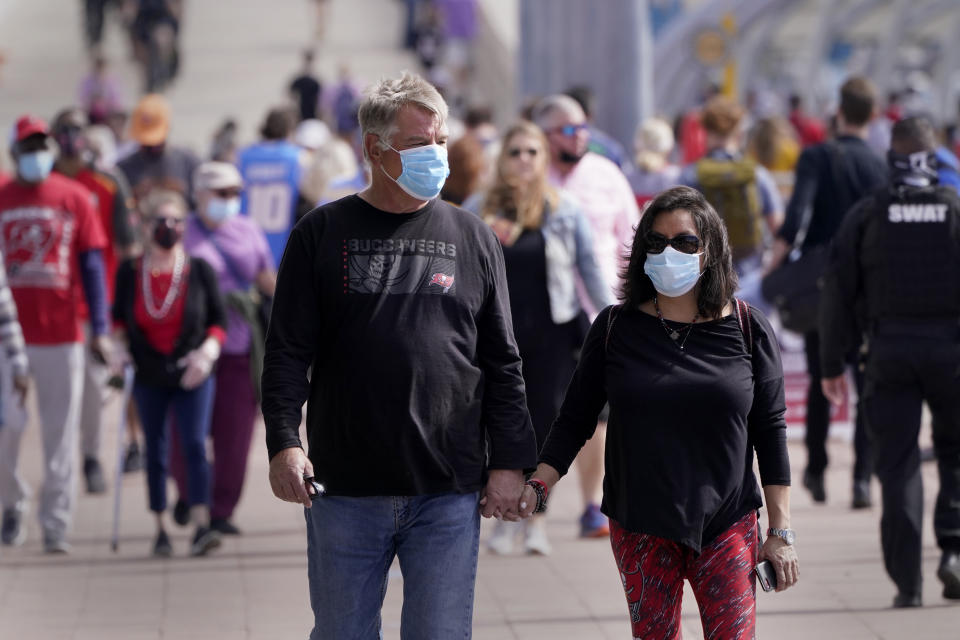 People wear masks as they walk down a sidewalk near Super Bowl 55 activities Friday, Feb. 5, 2021, in Tampa, Fla. The city is hosting Sunday's Super Bowl football game between the Tampa Bay Buccaneers and the Kansas City Chiefs. (AP Photo/Charlie Riedel)