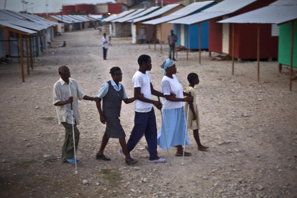 In this picture taken on Feb. 9, 2012, a child guides a group of blind people, displaced by the 2010 earthquake, in a single file, hand to arm, at La Piste camp in Port-au-Prince, Haiti. While more than a million people displaced by the 2010 quake ended up in post-apocalyptic-like tent cities, some of the homeless disabled population landed in the near-model community of La Piste, a settlement of plywood shelters along tidy gravel lanes. However, the rare respite for the estimated 500-plus people living at the camp is coming to an end as the government moves to reclaim the land. (AP Photo/Ramon Espinosa)