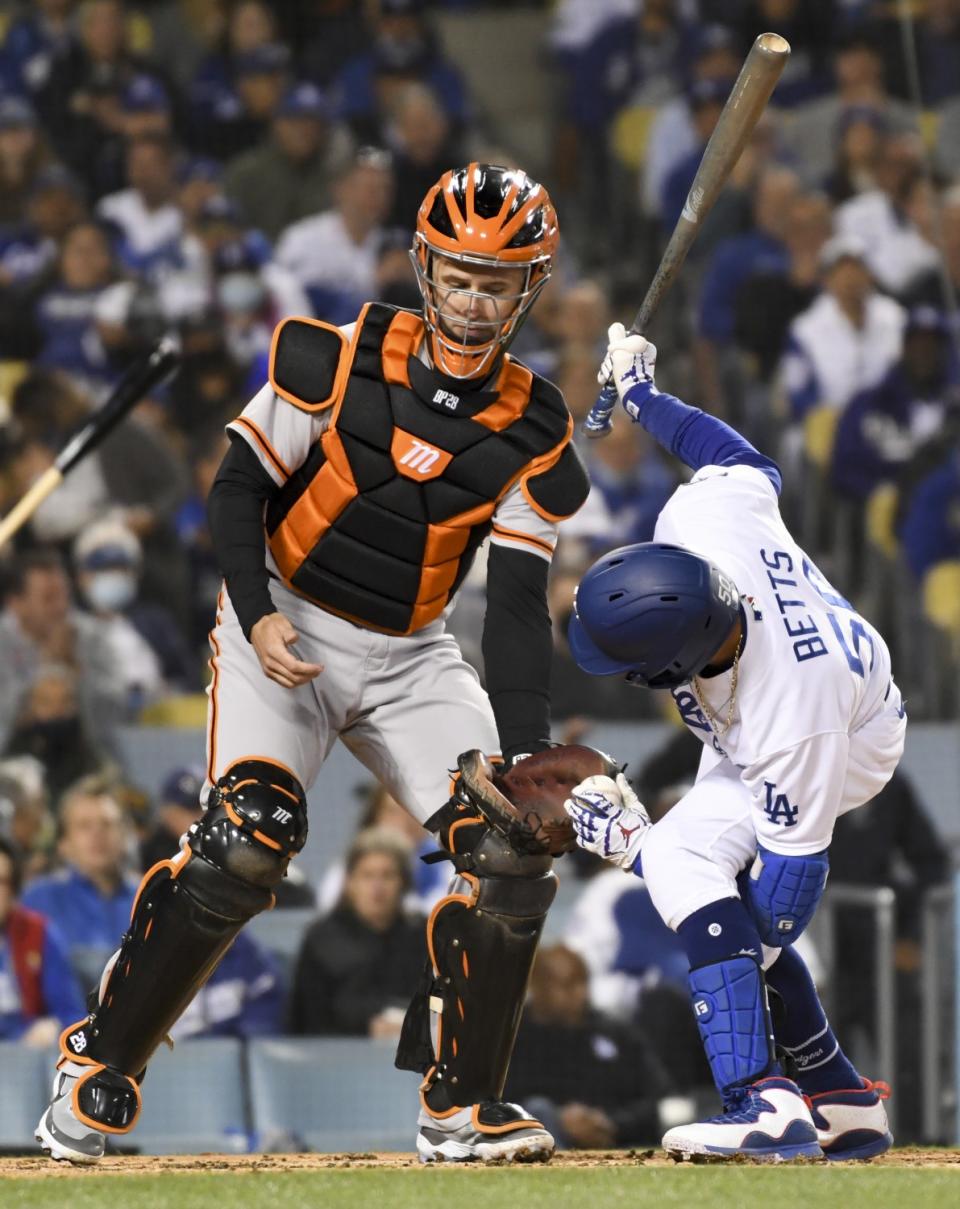 Dodgers' Mookie Betts hands the baseball between his legs to Giants catcher.