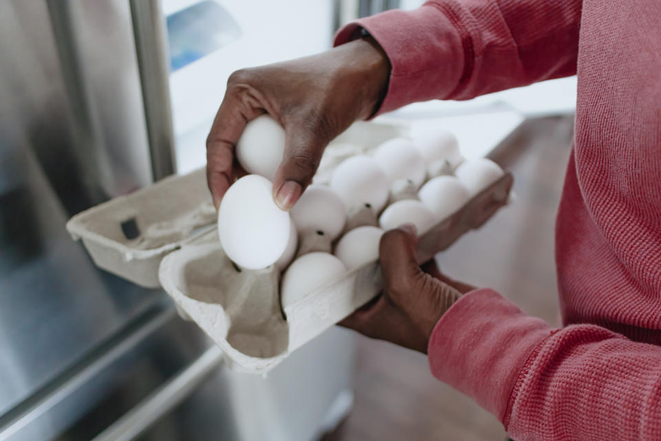 Person in a red long-sleeve shirt placing eggs into a carton in a kitchen