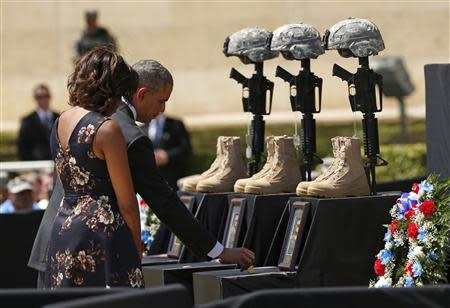 U.S. President Barack Obama places a challenge coin on a memorial as he and first lady Michelle Obama pay their respects for the dead soldiers at the conclusion of service in Fort Hood, Texas April 9, 2014. REUTERS/Kevin Lamarque