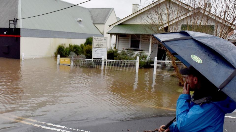 Man with umbrella looking at NSW flood damage