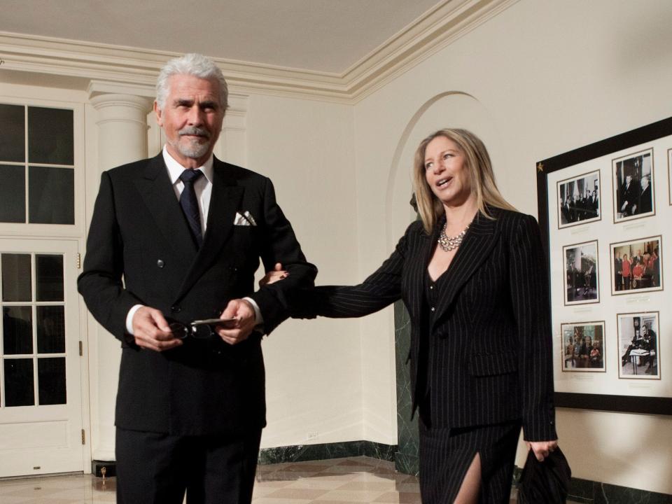 James Brolin, in a black suit, stands in the White House ahead of a state dinner along with wife Barbra Streisand, in a pinstriped jacket and dress, who's holding his arm.