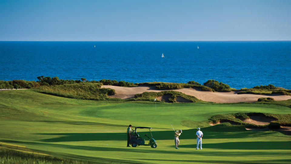 Golfers play a round at the Resort at Pelican Hill on a sunny day with blue skies and a view of the Pacific Ocean