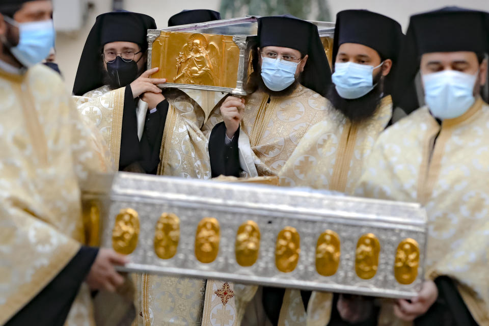 Priests, wearing masks against the COVID-19 infection, carry the remains of Saint Dimitrie Bassarabov, the patron saint of the Romanian capital, on the first of three days of pilgrimage, taking place at a much smaller scale than usual, due to the pandemic control imposed measures, in Bucharest, Romania, Sunday, Oct. 25, 2020. Romania's daily tally of coronavirus infections rose above 5,000 for the first time last week and patients in intensive care units also reached a new high. (AP Photo/Vadim Ghirda)