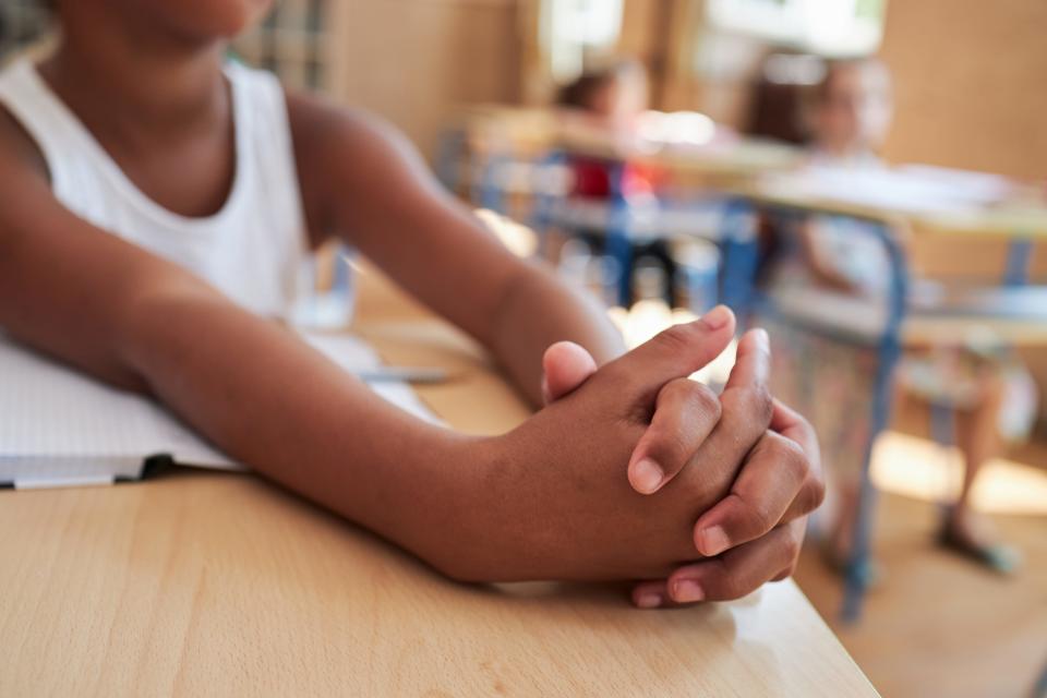 Close up of a nervous African-American schoolgirl hands while she answering to teacher questions for a mark