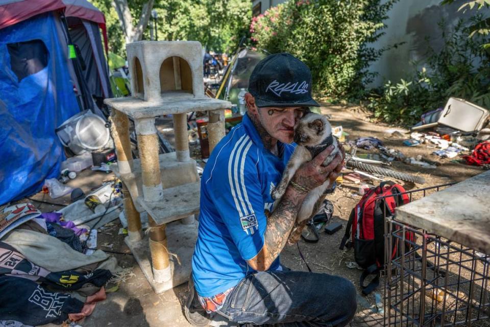 Robert Ash tries to calm his cat Meow Meow, who he said was frightened by the sound of the city’s disposal vehicles, during a homeless encampment sweep on C Street on Wednesday. He hauled his possessions, along with his wife’s belongings and their dog Sugar, a few blocks away because they were afraid they couldn’t sort their belongings quickly enough to avoid being trashed by the city’s crews.