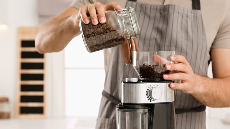 man using electric coffee grinder in kitchen