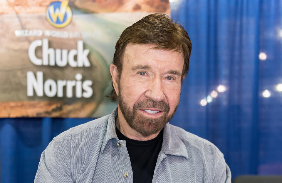 Chuck Norris poses in front of a banner that says "Wizard World Presents Chuck Norris"