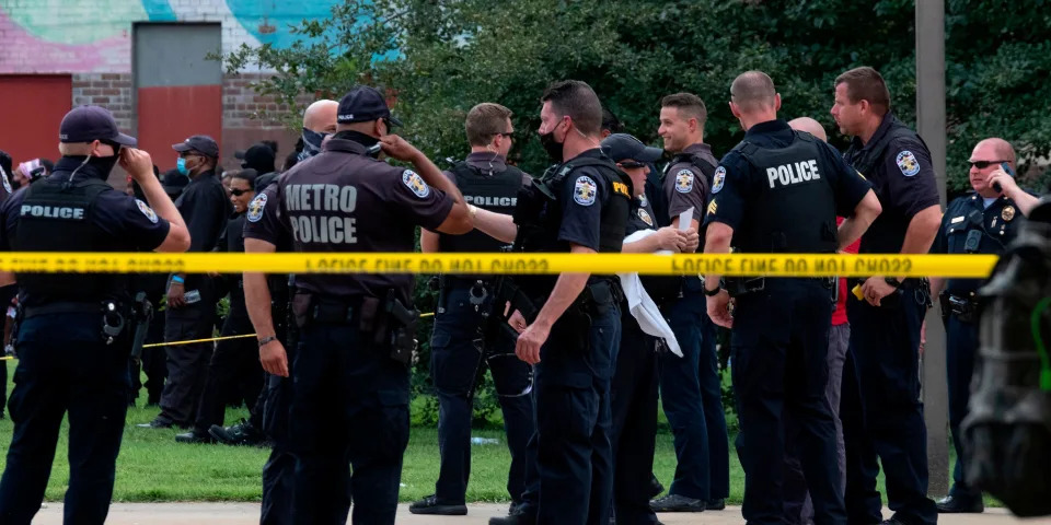 Louisville Metro Police Department members stand behind police caution tape.