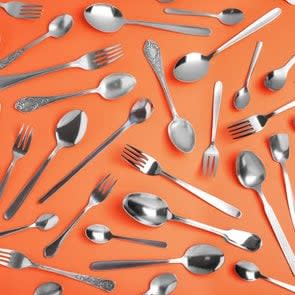 Set of new silver cutlery on coral background, flat lay