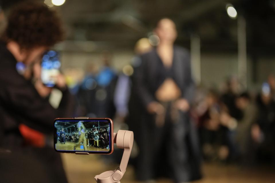 A guest records on a cell phone as models wear creations as part of the Tokyo James women's Fall-Winter 2023-24 collection presented in Milan, Italy, Saturday, Feb. 25, 2023. (AP Photo/Antonio Calanni)