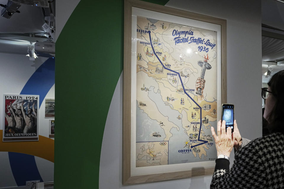 A woman photographs the torch roadmap of the 1936 Olympic Games, during an exhibition press day, Wednesday, March 27, 2024 in Paris. Ahead of this summer's Paris Olympics, an exhibit in the French capital shows how the Games have been a "mirror of society" since the beginning of the 20th century. (AP Photo/Laurent Cipriani)