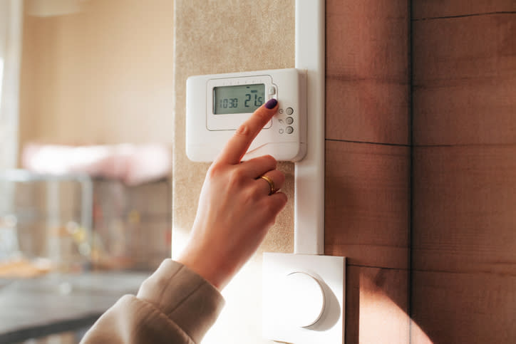 Person adjusting a digital thermostat on a wall