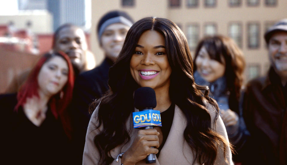 Gabrielle Union stands with a microphone with people behind her