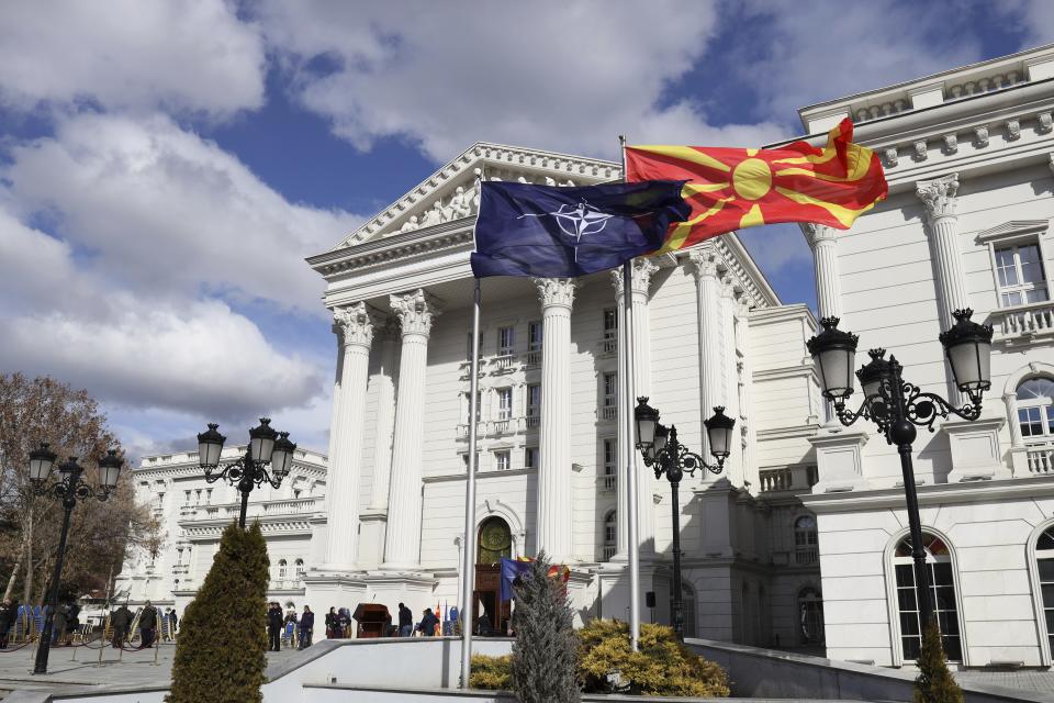 Macedonian, right, and NATO flag wave in front of the government building during a ceremony in Skopje, Tuesday, Feb. 12, 2019. Macedonian authorities began removing official signs from government buildings to prepare for the country's new name: North Macedonia. (AP Photo/Dragan Perkovksi)