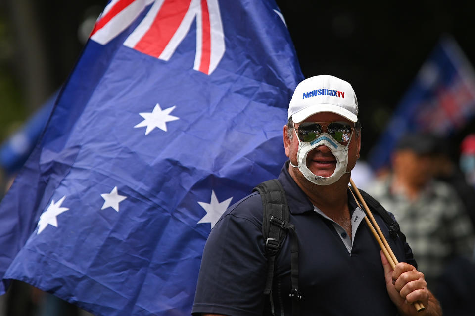 A man wearing a mask with a hole cut out of it holds an Australian flag during protest against mandatory vaccinations and lockdown measures in Sydney. Source: AAP