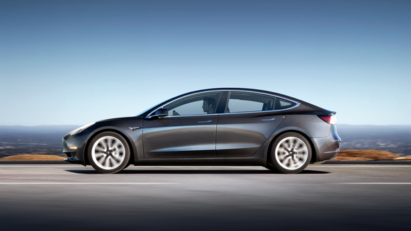 A gray Model 3 on a road next to a body of water