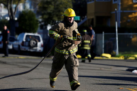 A firefighter carries a water hose near a warehouse where a fire broke out during an electronic dance party late Friday evening, resulting in at least nine deaths and many unaccounted for in the Fruitvale district of Oakland, California, U.S. December 3, 2016. REUTERS/Stephen Lam