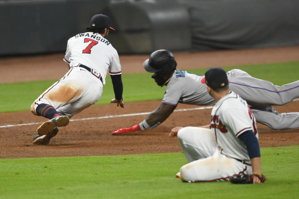 Atlanta Braves shortstop Dansby Swanson (7) moves in to tag out Miami Marlins' Monte Harrison, back right, at third base for a double play on a throw from first baseman Freddie Freeman as Braves relief pitcher Mark Melancon ducks in the foreground during the ninth inning of a baseball game Monday, Sept. 21, 2020, in Atlanta. (AP Photo/John Amis)