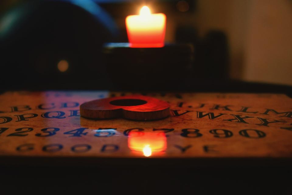 Heart Shaped Planchette On Ouija Board By Candle In Darkroom