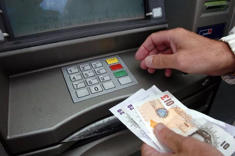 The hands of a man withdrawing money - in this case £50 in notes - from an ATM (automated teller machine) or cashpoint