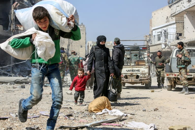 A Syrian boy carries sacks past government soldiers as civilians flee the Eastern Ghouta rebel enclave on March 17, 2018