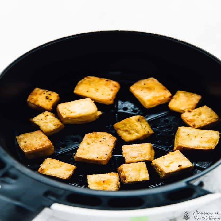 Tofu cubes cooking in an air fryer basket