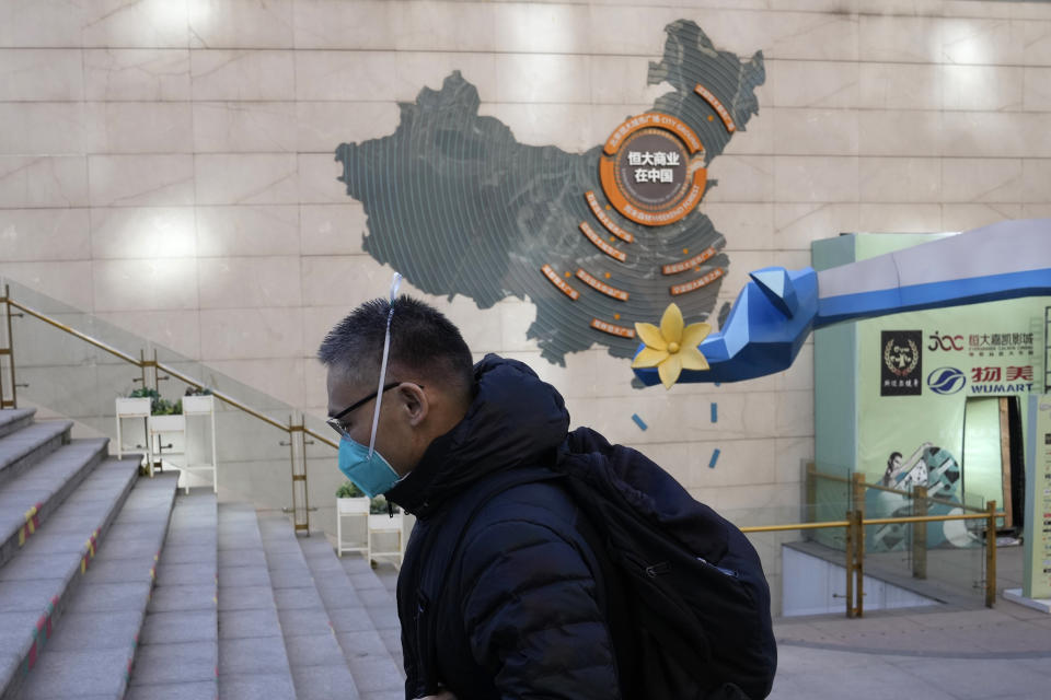 A man wearing a mask passes by a sign depicting Evergrande Group's China operation at a one of their commercial projects in Beijing, China, Tuesday, Dec. 7, 2021. Evergrande Group's struggle to turn assets into cash has prompted fear a default might chill Chinese lending markets and cause global shockwaves. Economists say the ruling Communist Party can prevent a credit crunch but it wants to avoid sending the wrong signal by bailing out Evergrande in the middle of a campaign to force companies to cut debt Beijing worries is dangerously high. (AP Photo/Ng Han Guan)