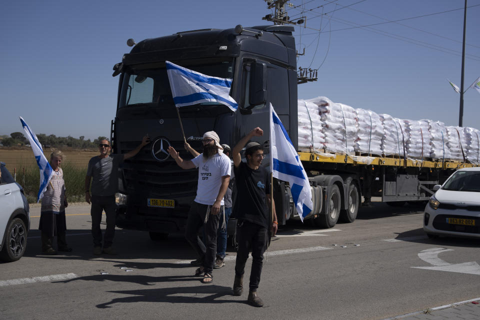 Holding Israeli flags people stand in front of trucks carrying humanitarian aid as they try to stop them to enter in the Gaza Strip in an area near the Kerem Shalom border crossing between Israel and Gaza, in southern Israel, in Kerem Shalom, Thursday, May 9, 2024. (AP Photo/Leo Correa)