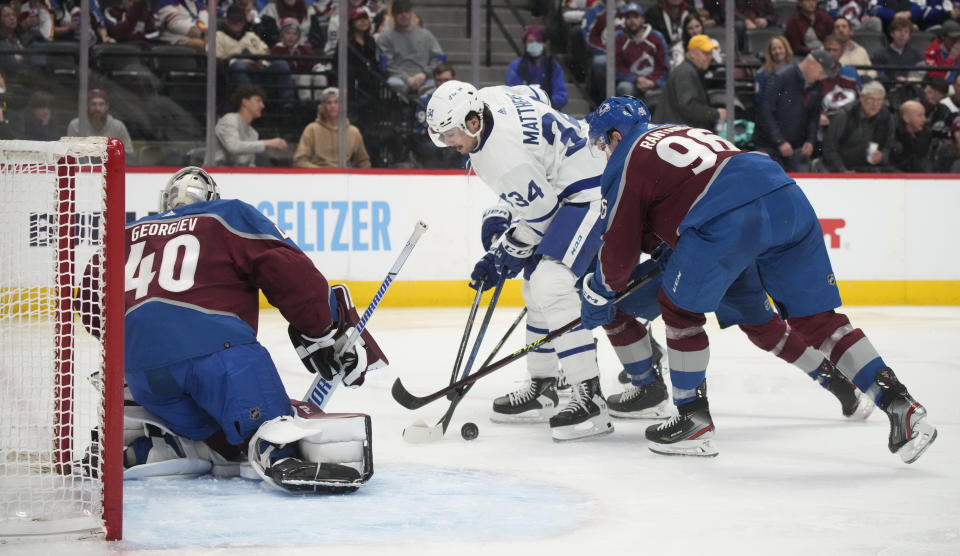 Toronto Maple Leafs center Auston Matthews, center, tries to redirect the puck at Colorado Avalanche goaltender Alexandar Georgiev, left, as Avalanche right wing Mikko Rantanen, right, defends in the second period of an NHL hockey game Saturday, Dec. 31, 2022, in Denver. (AP Photo/David Zalubowski)