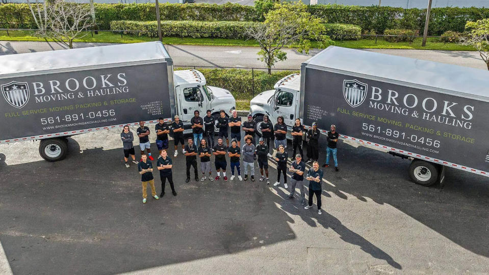 The Brooks Moving & Hauling team stands next to two of the company's moving trucks.