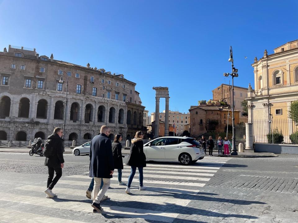 people crossing a busy street in rome near the colosseum