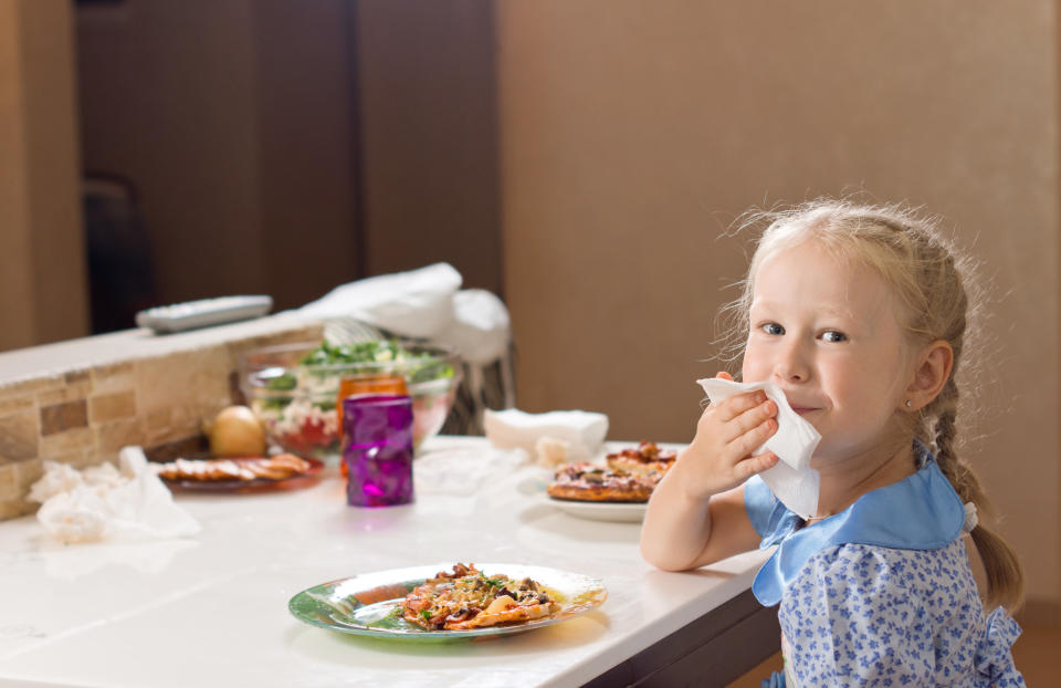 Girl wiping her mouth with a napkin at the dinner table