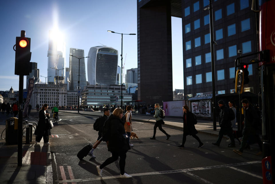 People cross the road on London Bridge during the morning rush hour, with the City of London's financial district in the background, in London, Britain, April 13, 2023. REUTERS/Henry Nicholls