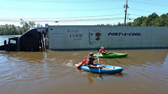 Anthony Writebol, left, and his cousin, Melissa Hill paddle past a stranded tractor trailer on Hwy 211 in Lumberton, N.C., Sunday, Oct. 9, 2016. They were heading to meet friends who were going to let them stay after their neighborhood "wayfarer" was flooded overnight by heavy rains associated with Hurricane Matthew. (Chuck Liddy/The Charlotte Observer via AP)