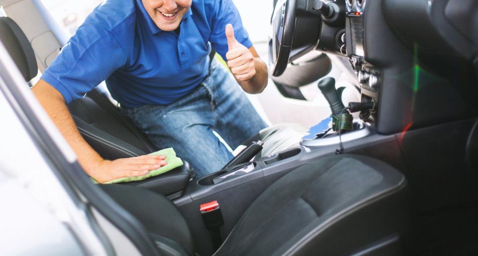 closeup of unrecognizable mid 30s caucasian man cleaning the interior of his car with a green dry cloth hes looking at camera and showing thumbs up hes wearing jeans and blue polo t shirtshot through passenger door ajar