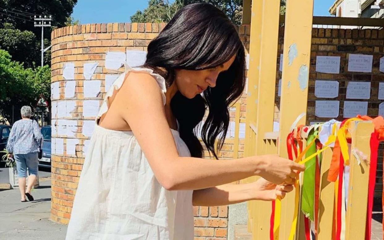 The Duchess of Sussex ties a ribbon at a memorial to University of Cape Town student Uyinene Mrwetyana at the post office where she was raped and murdered last month - PA