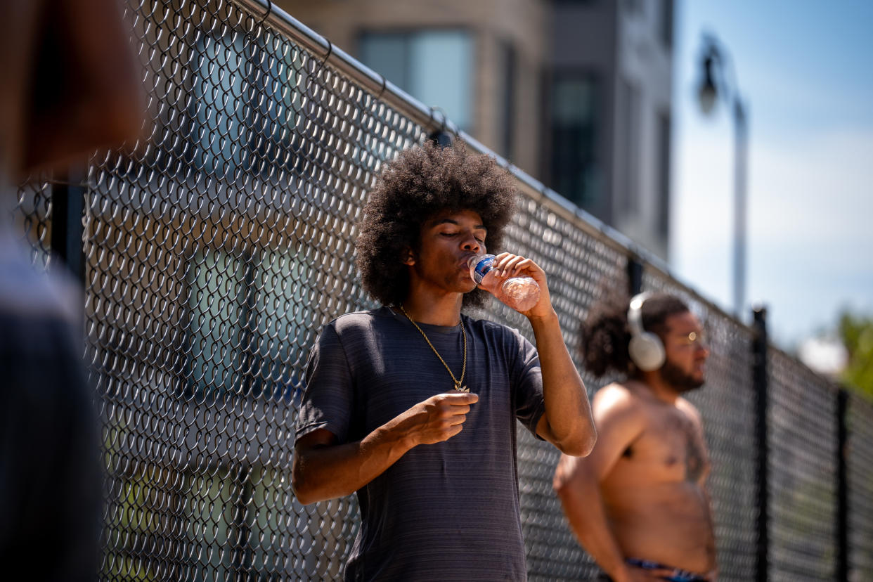 A man outside takes a drink from a plastic bottle.