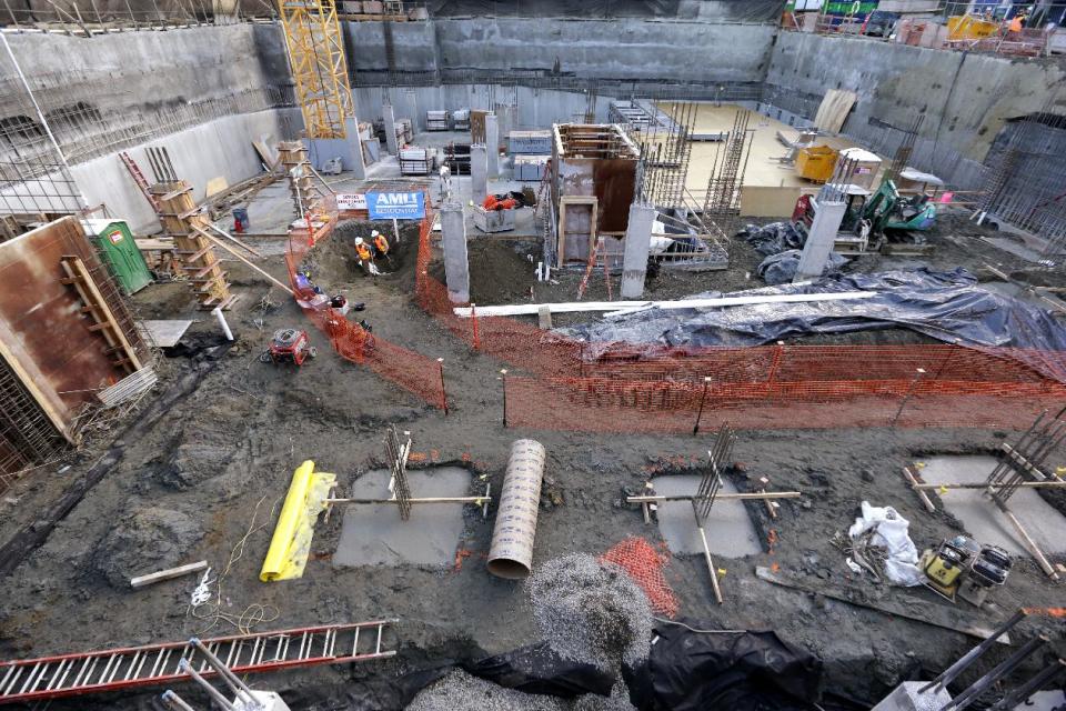 Researchers from the University of Washington's Burke Museum, center left, dig around a fossilized mammoth tusk that they've covered with a protective material at a building site Thursday, Feb. 13, 2014, in Seattle. In the crowded south Lake Union neighborhood where Amazon.com workers go out for espresso, an ice age mammoth died 10,000 years ago and remained until this week, when a plumbing contractor crew uncovered its tusk. Paleontologists with the Burke Museum are working with the building contractor to remove the tusk. (AP Photo/Elaine Thompson)