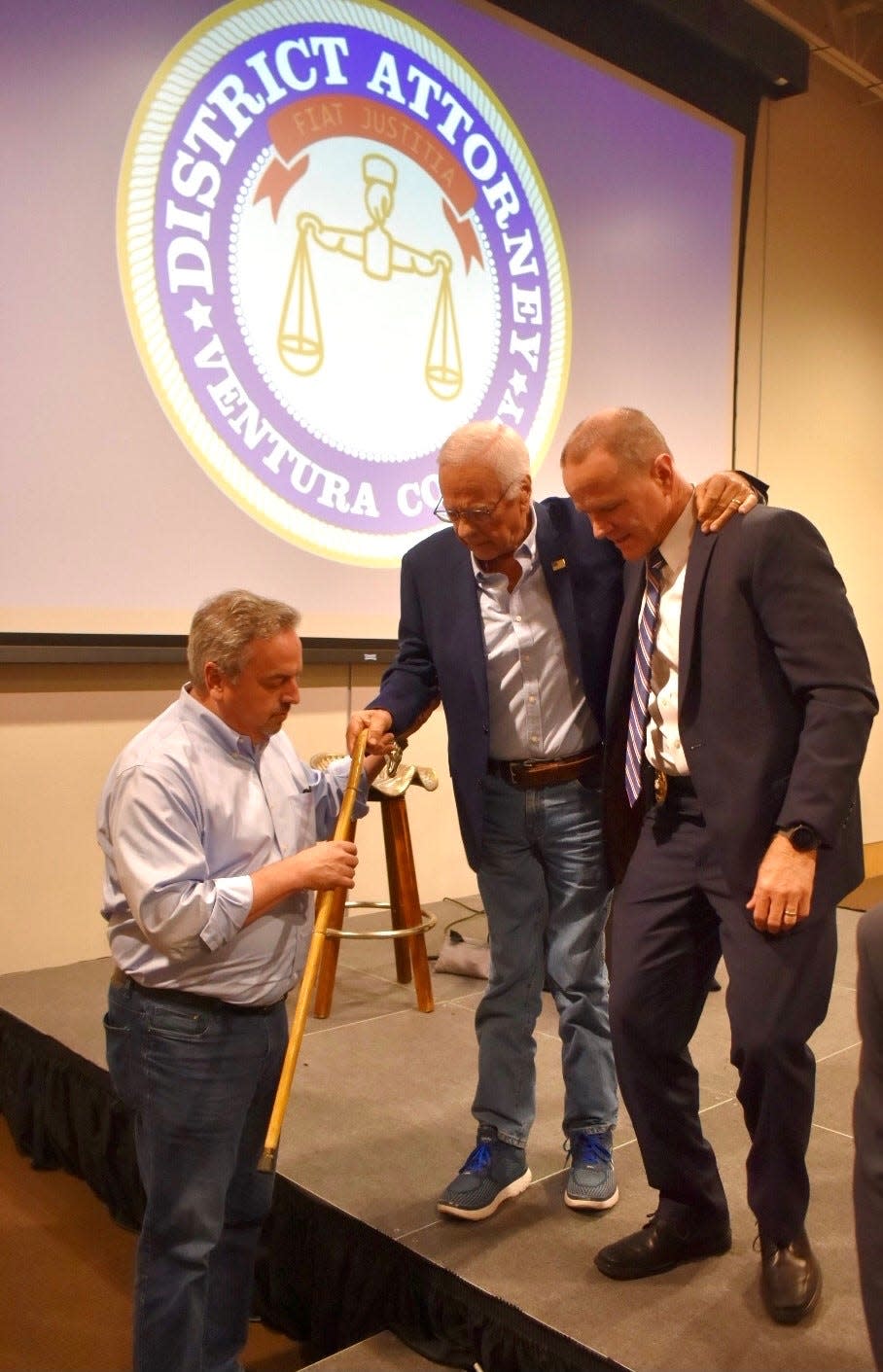 Former District Attorney Mike Bradbury is helped off the stage after a program at the Museum of Ventura County on May 3. Bradbury was diagnosed 20 years ago with a muscle deterioration disease called myositis.