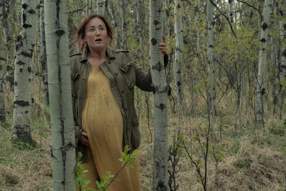 ellie's mom in the last of us. she's very pregnant and holding her belly, while wering a dirty yellow maxi dress and battered green goat. she's resting against a tree