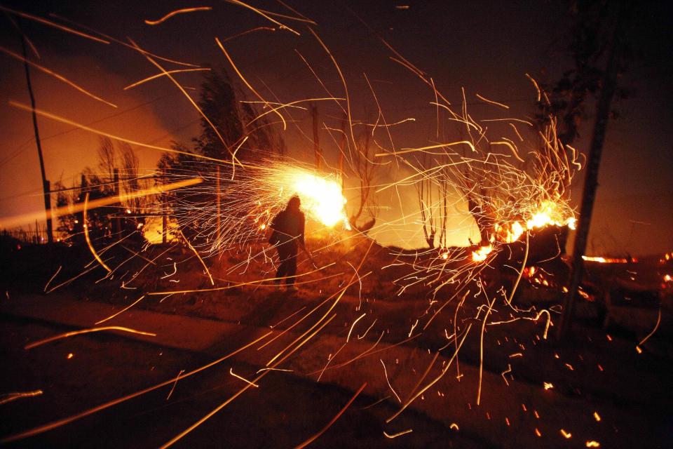 A person tries to extinguish flames as sparks fly during a wild forest fire in Valparaiso, Chile, Sunday April 13, 2014. Authorities say the fires have destroyed hundreds of homes, forced the evacuation of thousands and claimed the lives of at least seven people. ( AP Photo/ Luis Hidalgo)