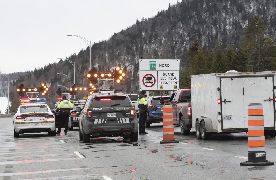 Police stop motorists at a checkpoint as Highway 175 is closed, Sunday, March 29, 2020, north of Quebec City. Highway 175 heading to the Saguenay region is closed to help prevent the spread of the new coronavirus pandemic. Only essential services and residents of the region are allowed through. (Jacques Boissinot/The Canadian Press via AP)