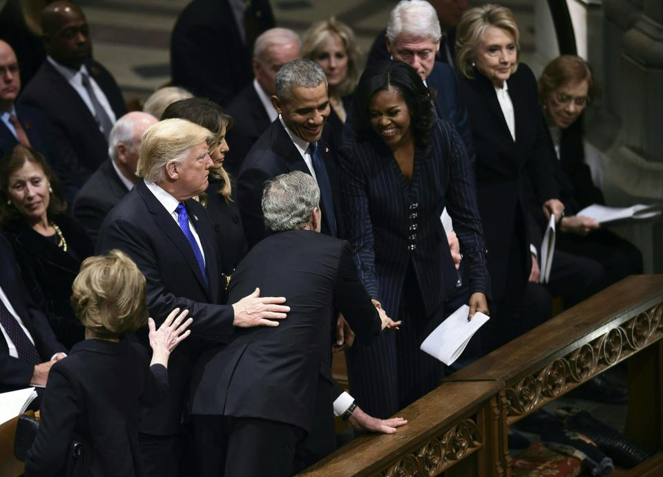 Former president George W. Bush (C), flanked by his wife Laura (bottom L)  reaches past (from L-R) US President Donald Trump, First Lady Melania and former president Barack Obama to give former first Lady Michelle Obama something as US president Bill Clinton and Hillary Clinton, and former president Jimmy Carter and Rosalynn Carter look on during the funeral service former president George H.W.Bush at the Washington National Cathedral in Washington, D.C.