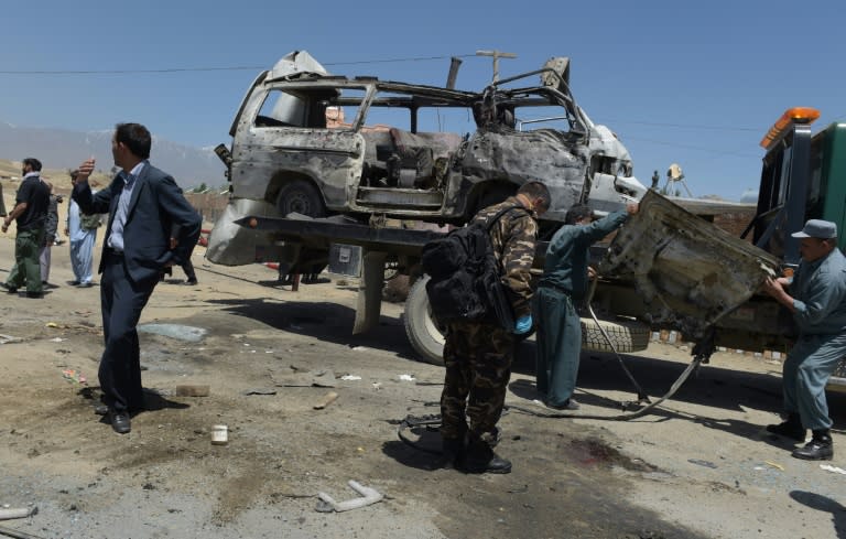 Afghan security personnel stand near damaged vehicles at the scene of a suicide bomb attack in Paghman district in Kabul on May 25, 2016