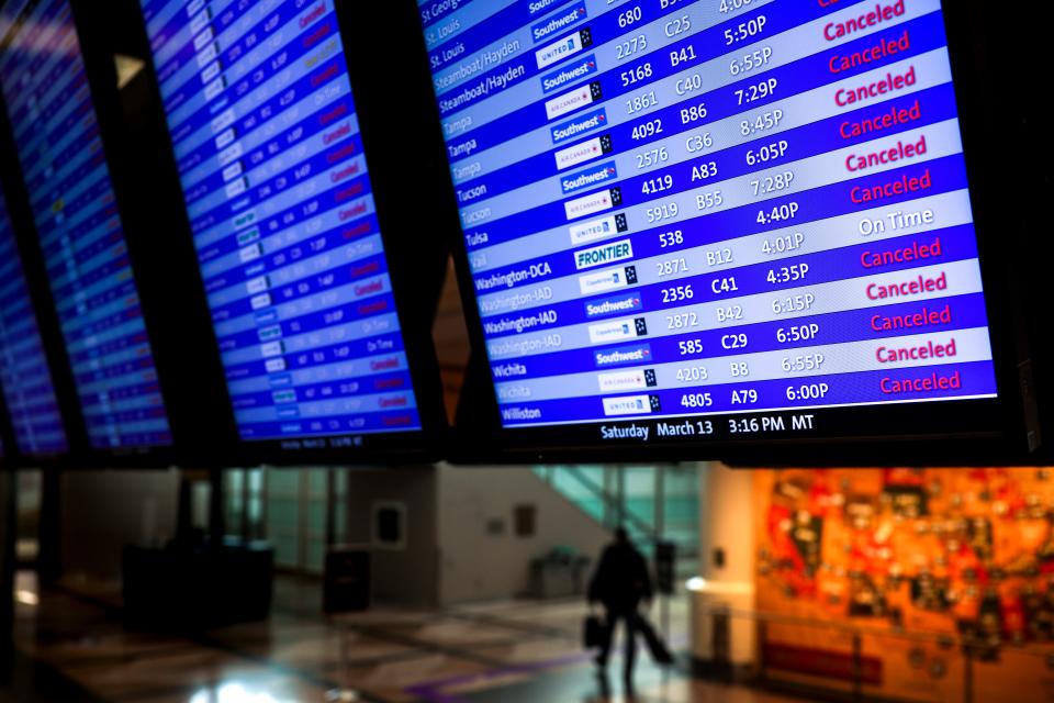 A man walks past a display board showing mostly canceled flights at Denver International Airport on March 13, 2021.