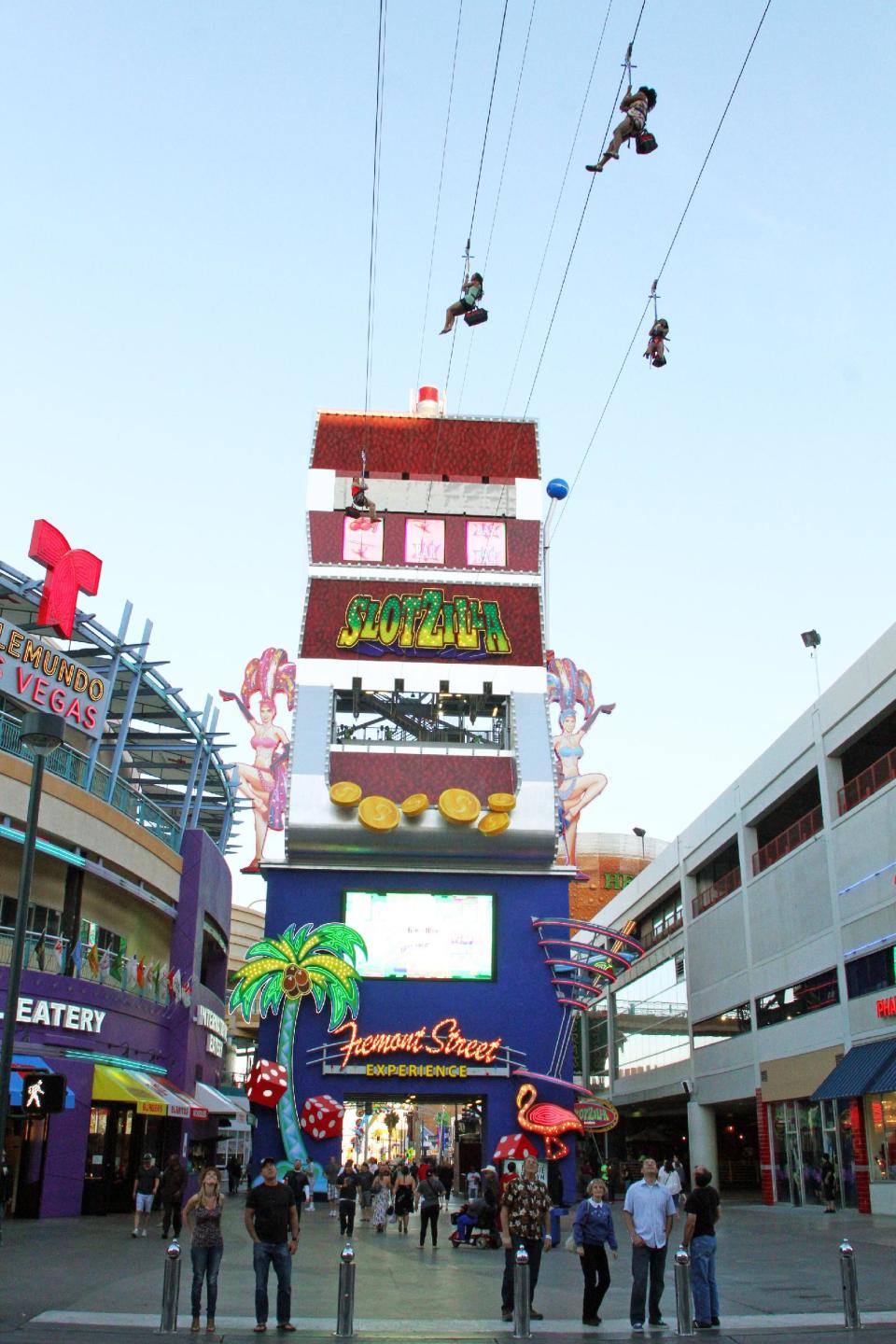 In this April 27, 2014 photo provided by the Fremont Street Experience, guests ride zip lines that swoop past the vintage casinos of downtown Las Vegas and under the giant video canopy of the Fremont Street Experience. The lower zip lines on the $12 million SlotZilla attraction opened over the weekend of April 26 after 14 months of construction. Rides start from a 12-story tower designed like a giant slot machine. Riders can now take the 77-foot-high zip lines, which harness visitors in a sitting position and take them 850 lateral feet to a platform near the 3rd Street Stage. (AP Photo/Fremont Street Experience, Scott Roeben)