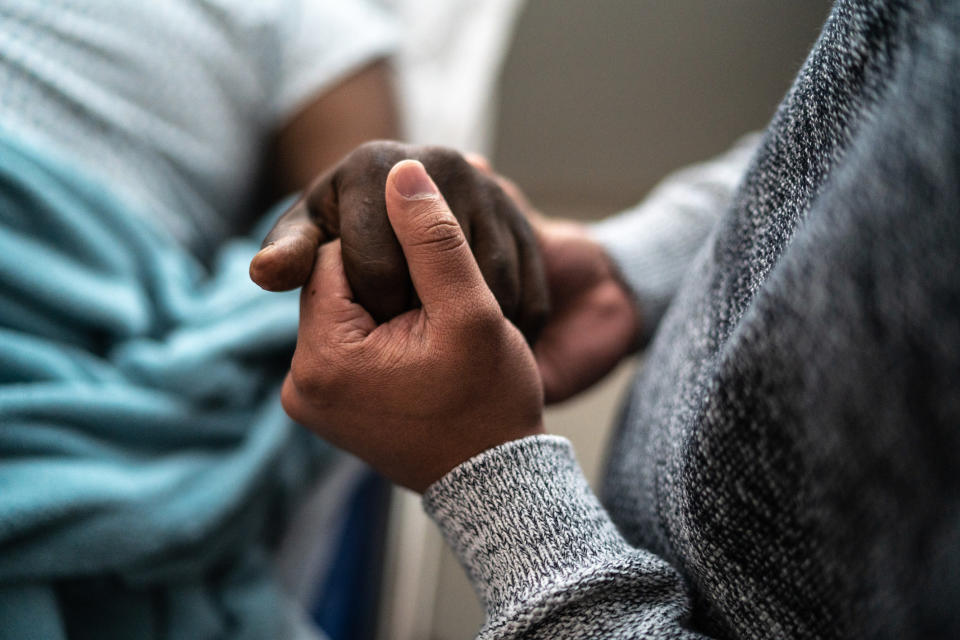 A person in a hospital bed holding hands with someone